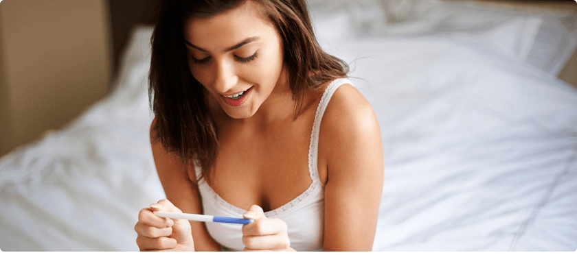A woman looking at a pregnancy test result with a happy face