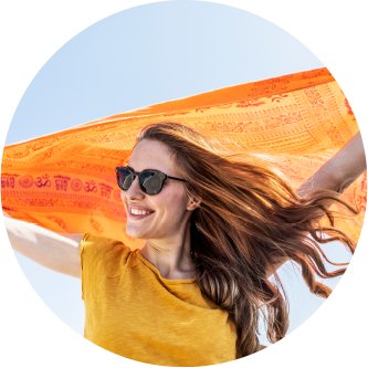 Smiling red haired woman in orange tee-shirt and sunglasses, holding up orange scarf in wind