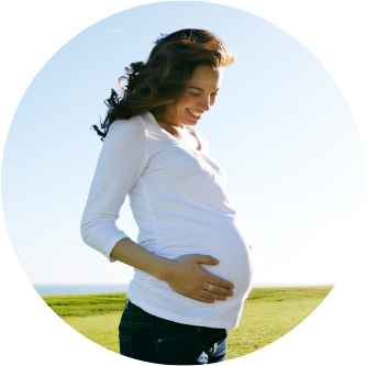 Pregnant woman standing outdoors and smiling at baby bump