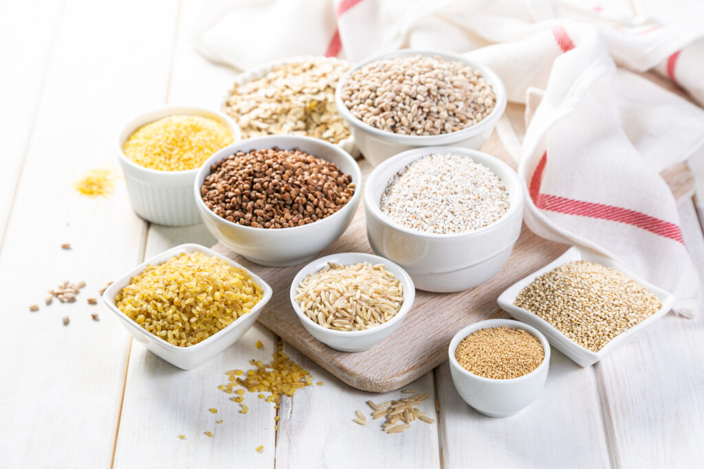 Selection of whole grains in white bowls - rice, oats, buckwheat, bulgur, porridge, barley, quinoa, amaranth,