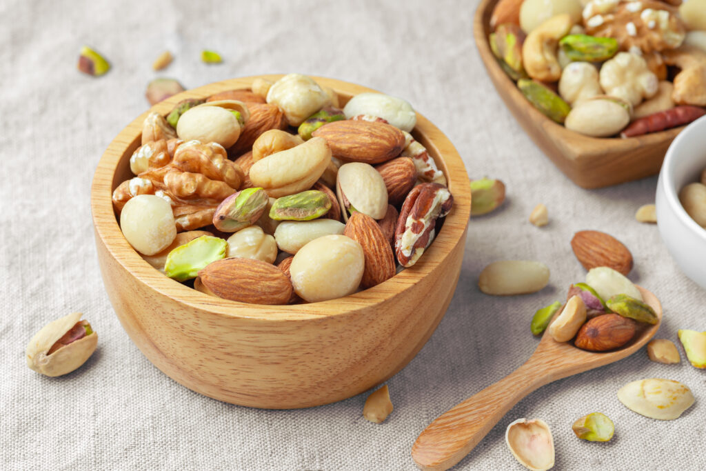 Various nuts in wooden bowl with spoon on linen tablecloth